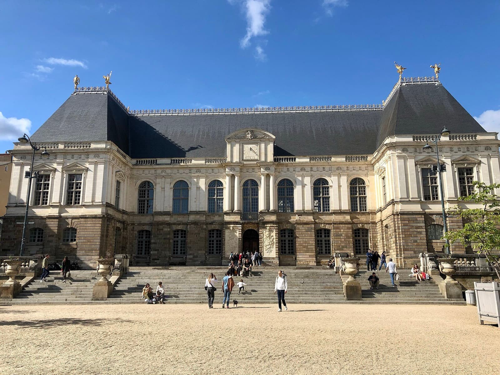 Le palais du Parlement de Bretagne à Rennes, sous un ciel bleu, avec des passants sur les marches